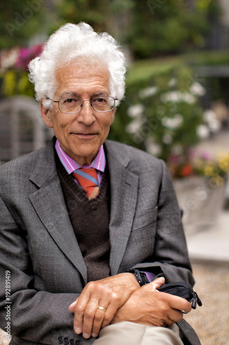 Old Man With White Hair And A Happy Expression Sitting In A Garden