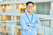 © Seventyfour - Waist up portrait of cheerful Asian businessman wearing glasses smiling happily at camera standing at glass balcony in modern office building, copy space