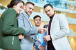© Seventyfour - Low angle portrait of modern businessman holding smartphone showing something to group of colleagues standing in hall of office building