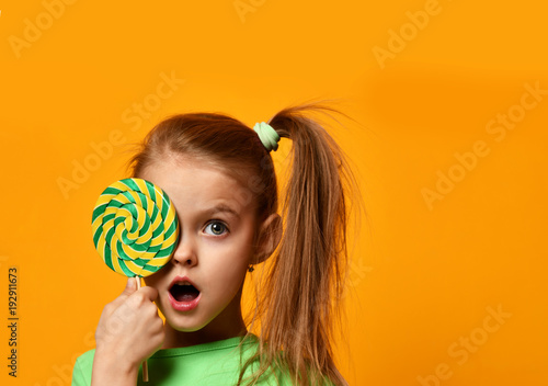 Fotografie, Obraz Happy young little child girl kid bite sweet lollypop candy