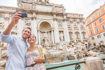 Wall Mural - Rome travel tourists couple at Trevi Fountain in Rome, Italy vacation. Happy young romantic couple traveling in Europe taking self-portrait with smartphone camera. Man and woman happy together