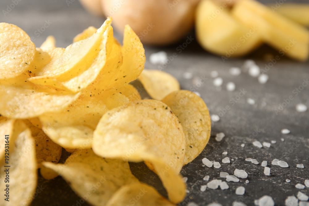 Yummy crispy potato chips with salt on grey table
