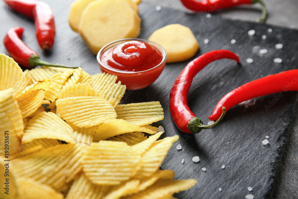 Crispy potato chips with chili pepper and sauce on slate plate, closeup