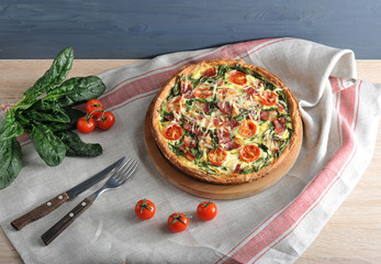 Classic French pie quiche with spinach, bacon, cherry tomatoes. In the frame cutlery, tomatoes, spinach. The background is draped with a napkin. Close-up. 