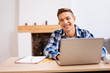 © zinkevych - Being inspired. Handsome cheerful fair-haired boy smiling and working on his laptop while sitting at the table