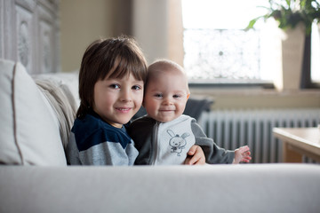 Wall Mural - Little baby boy and his older brother, sitting on a couch in sunny living room