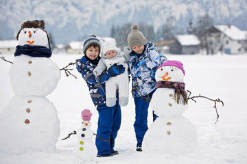 Poster - Family with children, building snowman in the park in little village in Austria