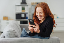 Young Cheerful Woman Using Mobile Phone On Sofa