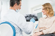 © LIGHTFIELD STUDIOS - Woman consulting with dentist looking at x-ray in modern clinic