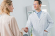© LIGHTFIELD STUDIOS - Smiling doctor and female patient shaking hands in modern dental clinic
