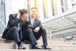 © khwanchai - desperate and unemployed people, Economic downturn concept, frustrated businessman sitting on stair, walkway after finding no job and friend helping and encourage for work and busines.