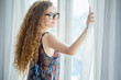 © iammotos - Beautiful woman opening curtains and looking through the window and enjoying a new day with a warm light from outdoors