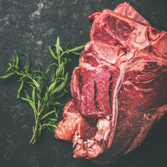 Wall Mural - Close-up of fresh raw beef meat t-bone steaks placed in stack with rosemary over black stone background, selective focus, copy space, square crop