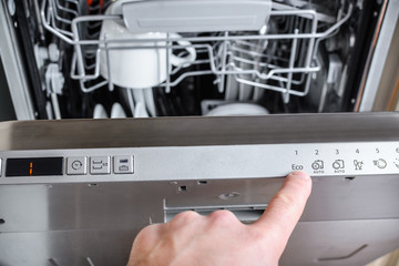 man chooses an eco program on the control panel of the dishwasher.