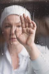 Wall Mural - close-up view of sick mature woman in kerchief touching window with raindrops