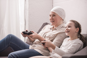 Wall Mural - side view of smiling grandmother and granddaughter playing with joysticks, cancer concept