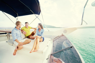 Wall Mural - Friendship and vacation. Group of laughing young people sitting on the yacht deck sailing the sea.