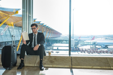 handsome businessman reading a book in the airport sitting close to the window