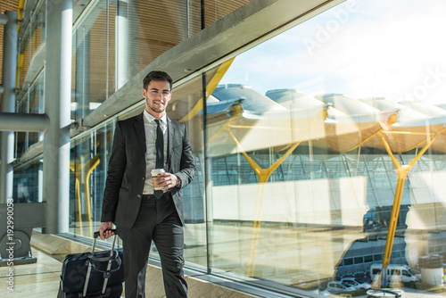 Plakat przystojny biznesmen stoi czekając na swój lot na lotnisku w pobliżu okna terminala