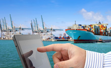 Man Analyzing Financial Data And Charts On Computer Screen, In The Background Container Terminal With Cargo Ship