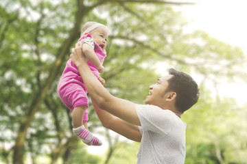 Wall Mural - Father lifting daughter with blur tree background