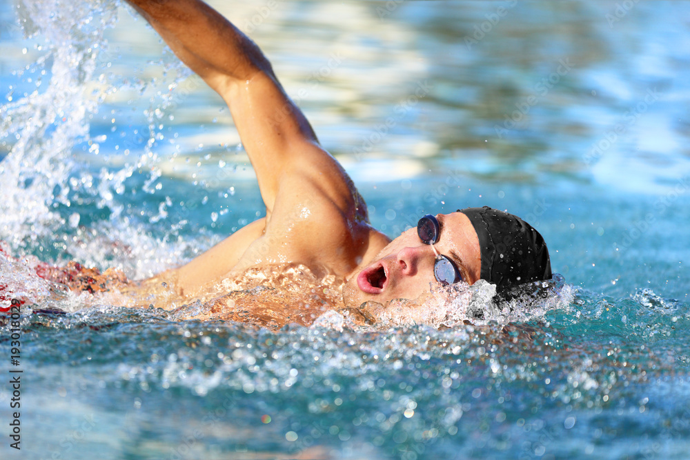 Man swimmer swimming crawl in blue ocean open water. Portrait of an athletic young male triathlete swimming crawl wearing cap and swimming goggles. Triathlete training for triathlon. - obrazy, fototapety, plakaty 