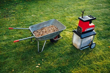 garden chipper, electric shredder (mulcher) with wheelbarrow full of wooden mulch, green grass background