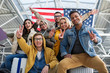 © Yakobchuk Olena - Low angle of happy men and women standing at the airport with banner of the united states and showing two finger gesture