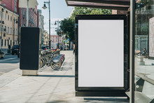 Vertical Blank White Billboard At Bus Stop On City Street. In The Background Buildings And Road. Mock Up. Poster On Street Next To Roadway. Sunny Summer Day.
