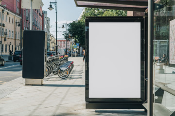 vertical blank white billboard at bus stop on city street. in the background buildings and road. moc
