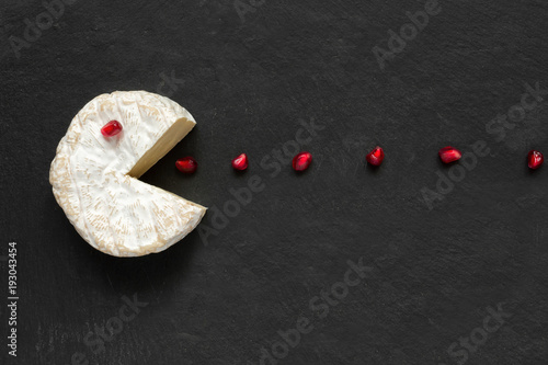 Fotografie, Obraz Camembert or brie cheese cut out like pacman eating pomegranate seeds on black s