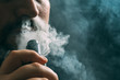 Man vaping e-cigarette with e-liquid, close-up, breathes out large cloud of vapor. Vape concept