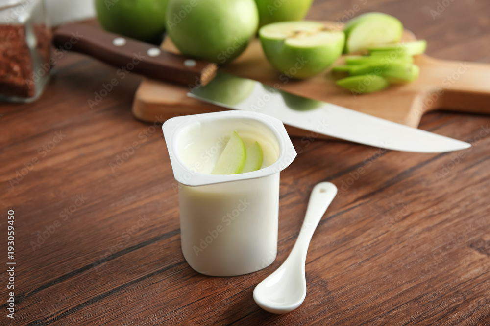 Plastic cup of yummy apple yogurt on wooden table