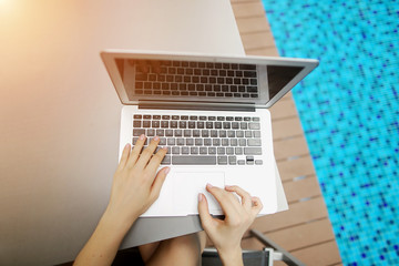 Wall Mural - view from above of woman hands pressing buttons on laptop at sunny day swimming pool. concept of business freelance working, new technologies. Fingers typing on the computer keyboard