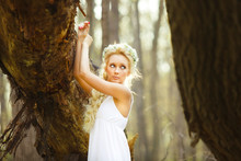 Blond Woman Stands In White Dress By Tree.