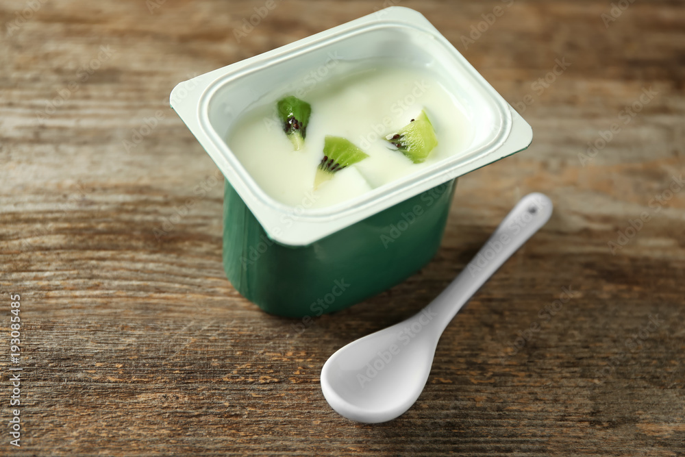 Plastic cup with yummy kiwi yogurt on wooden table