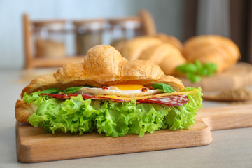 Poster - Wooden board with tasty croissant sandwich on table