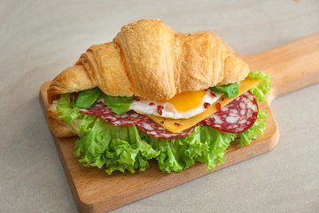 Poster - Wooden board with tasty croissant sandwich on table