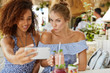 Cheerful women lesbians make selfie on modern mobile phone, drink smoothie, enjoy wireless internet connection for making video call, communicate with friends or blogg online. Technology concept
