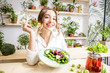 Portrait of a young woman eating healthy food sitting in the beautiful interior with green flowers on the background