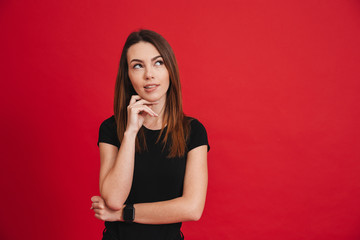 Sticker - Portrait of young woman 20s wearing black looking upward and touching chin with brooding or dreaming view isolated over red background