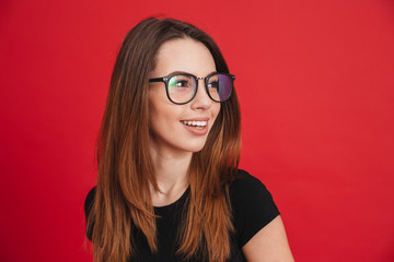 Closeup photo of young stylish woman 20s wearing black t-shirt and eyeglasses looking aside with wonderful smile isolated over red background