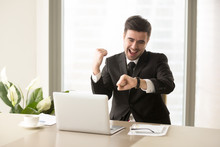 Excited Businessman Yelling With Joy When Sitting At Desk In Front Of Laptop And Looking At Wrist Watch. Happy Office Worker Finishing Work Before Deadline, Glad Because Of Ending Of Working Day