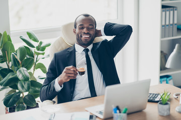 Attractive, cheerful lawyer enjoying break time, having fun, holding hand behind the head, mug with coffee, watching his favorite program on laptop, sitting at desk