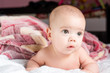 Beautiful happy small baby girl lying in bed and looking with smile. Closeup portrait