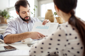 Poster - Look here. Attractive concentrated bearded man holding a sheet of paper and showing a diagram to his partner sitting opposite him