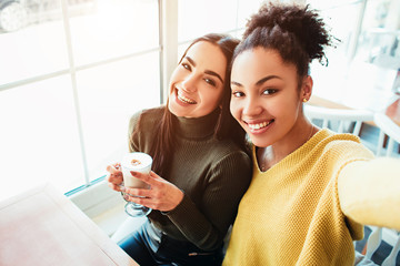 This is a selfie of two beautiful girls that look so amazing and happy at the same time. They are in cafe drinking some coffee end enjoying time spending together. Close up. Cut view.