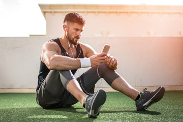 Young handsome man using phone while having exercise break in rooftop gym.