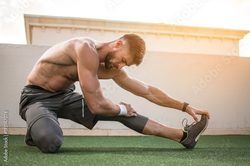 Fotografía Muscular shirtless sportsman stretching legs before morning workout