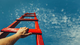 Fototapeta  - Development Attainment Motivation Career Growth Concept. Mans Hand Reaching For Red Ladder Leading To A Blue Sky